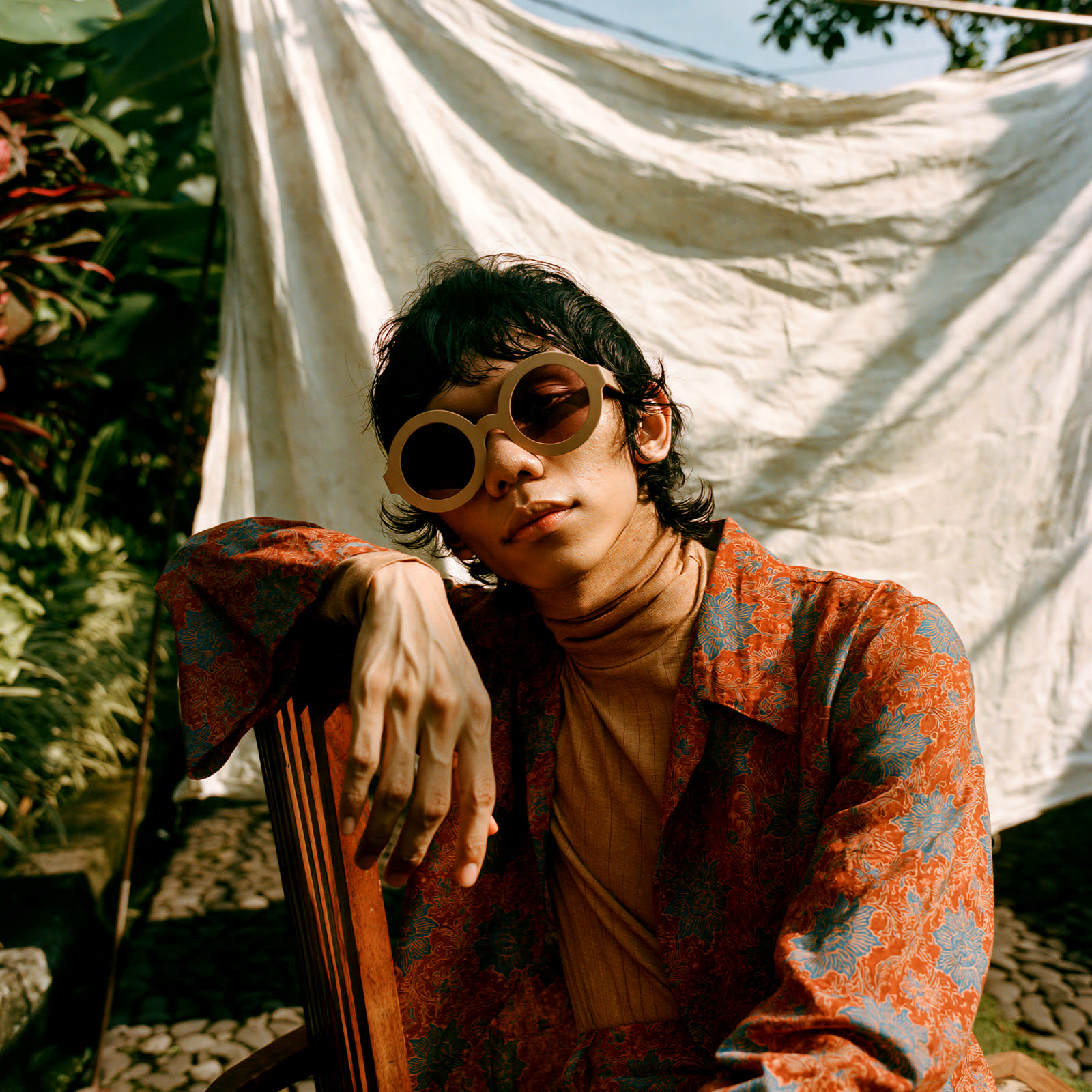 A man draped over a chair back in cream round sunglasses