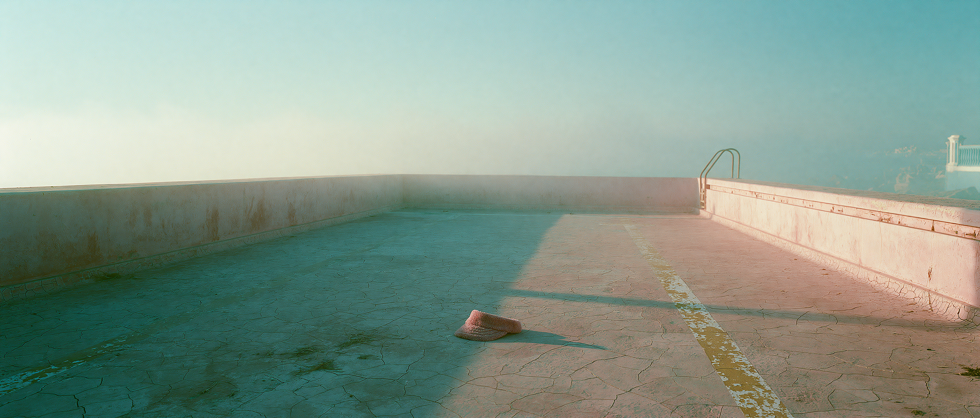 An empty cracked pool basin in golden haze, a single slide left on the floor