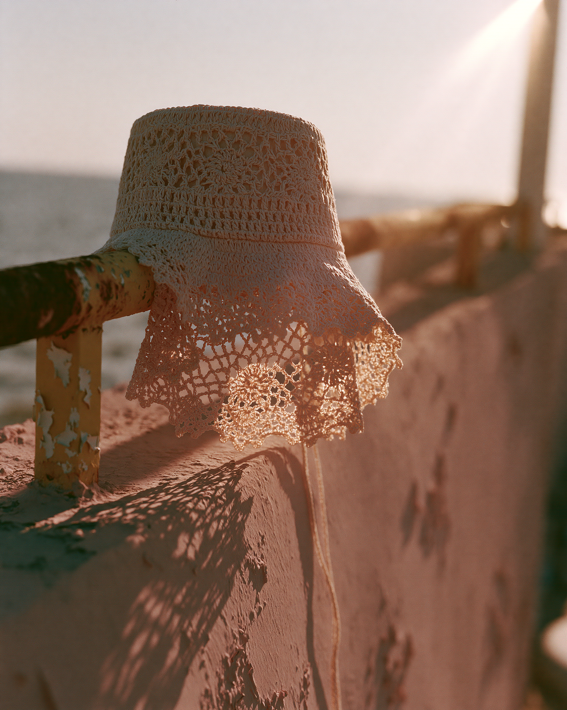 A crochet cream bucket hat resting on a rusted yellow rail in low sun