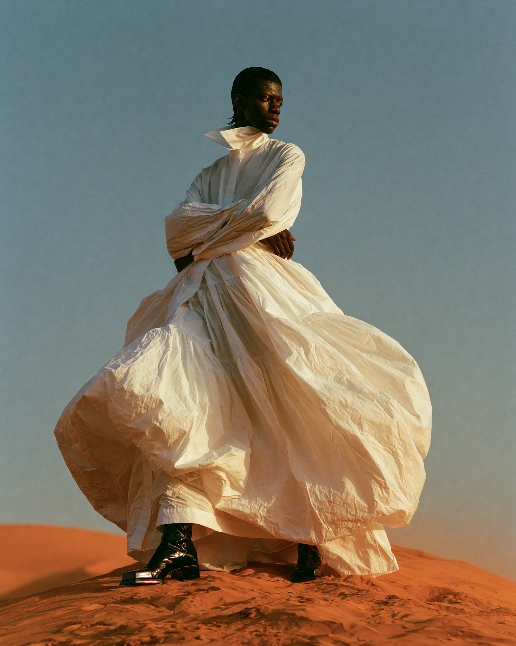 Model in a wind-filled white gown on a red dune