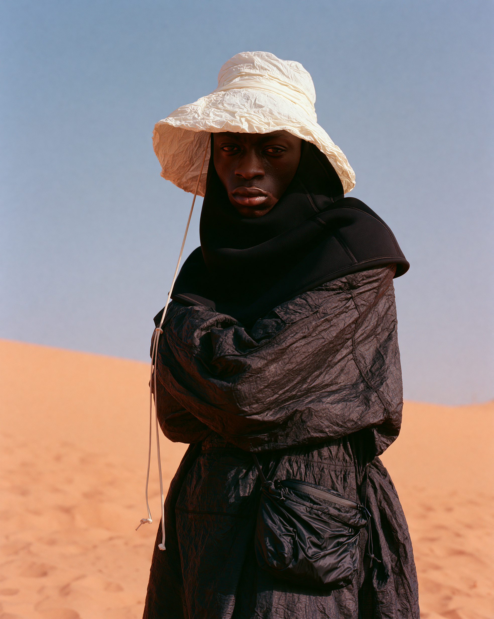 Model in a white hat and black quilted coat against the sand