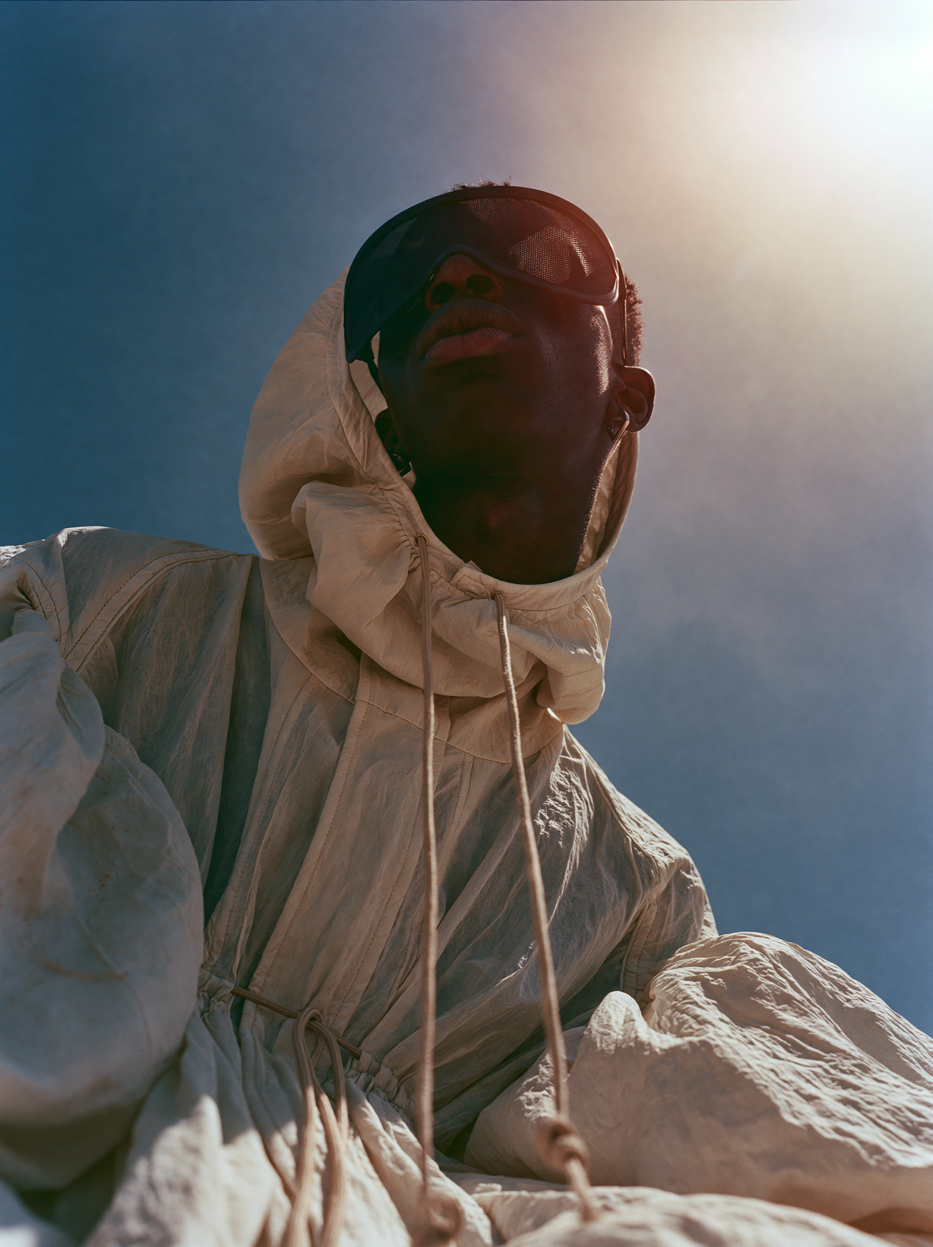 Low-angle portrait of a hooded figure, the sun flaring behind