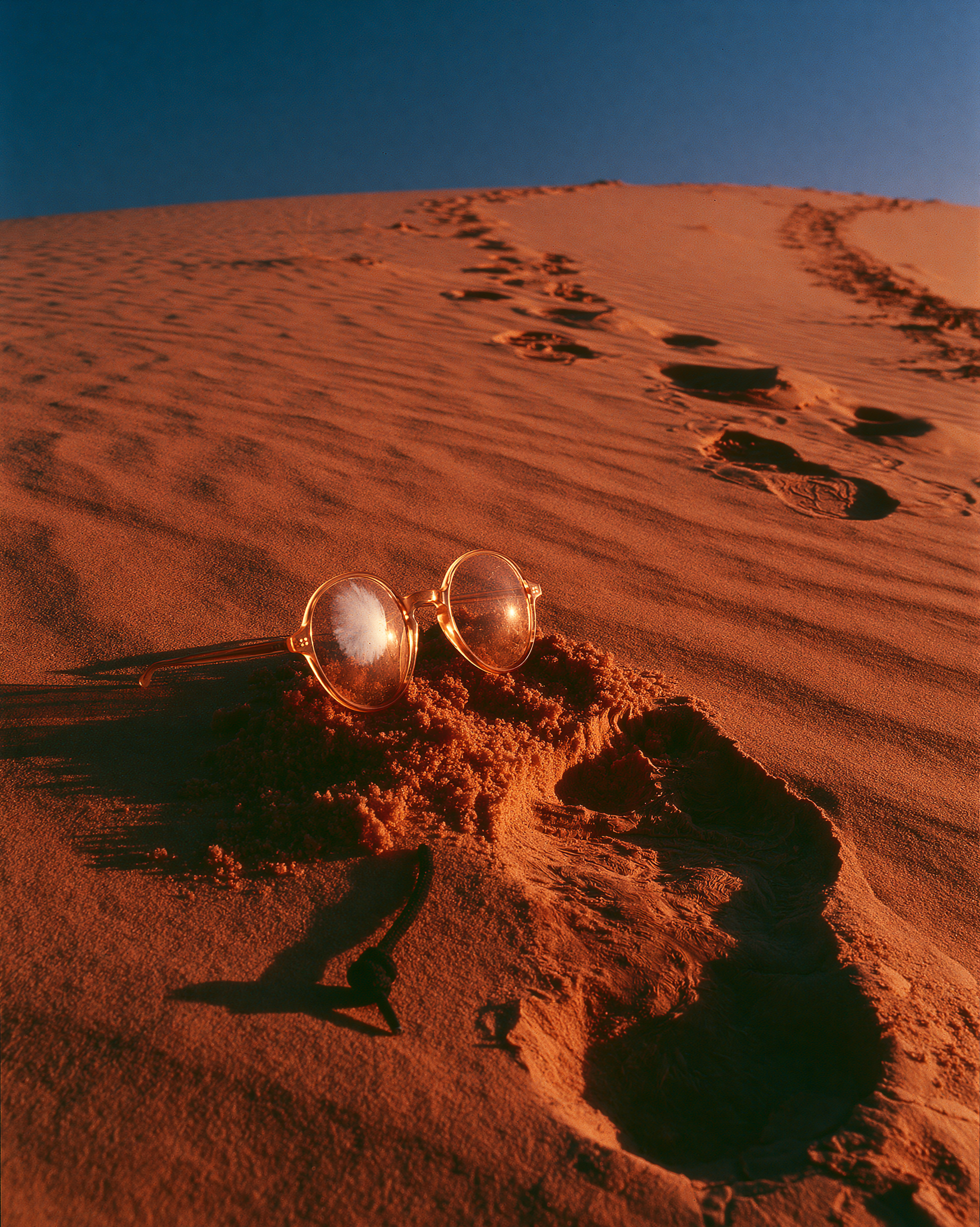 Abandoned amber glasses and a trail of footprints up a dune at sunset