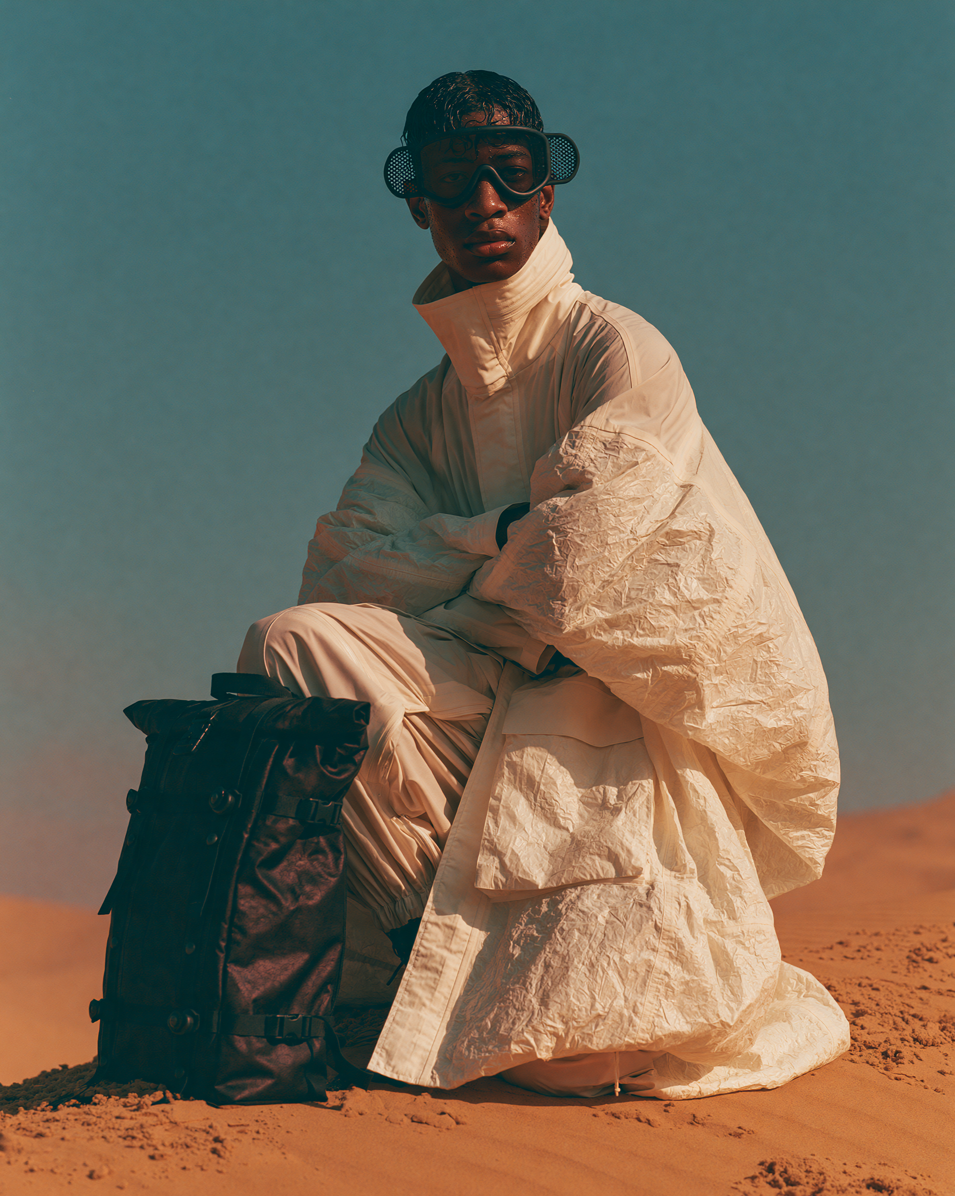 A crouching figure in white tactical gear and goggles on a dune