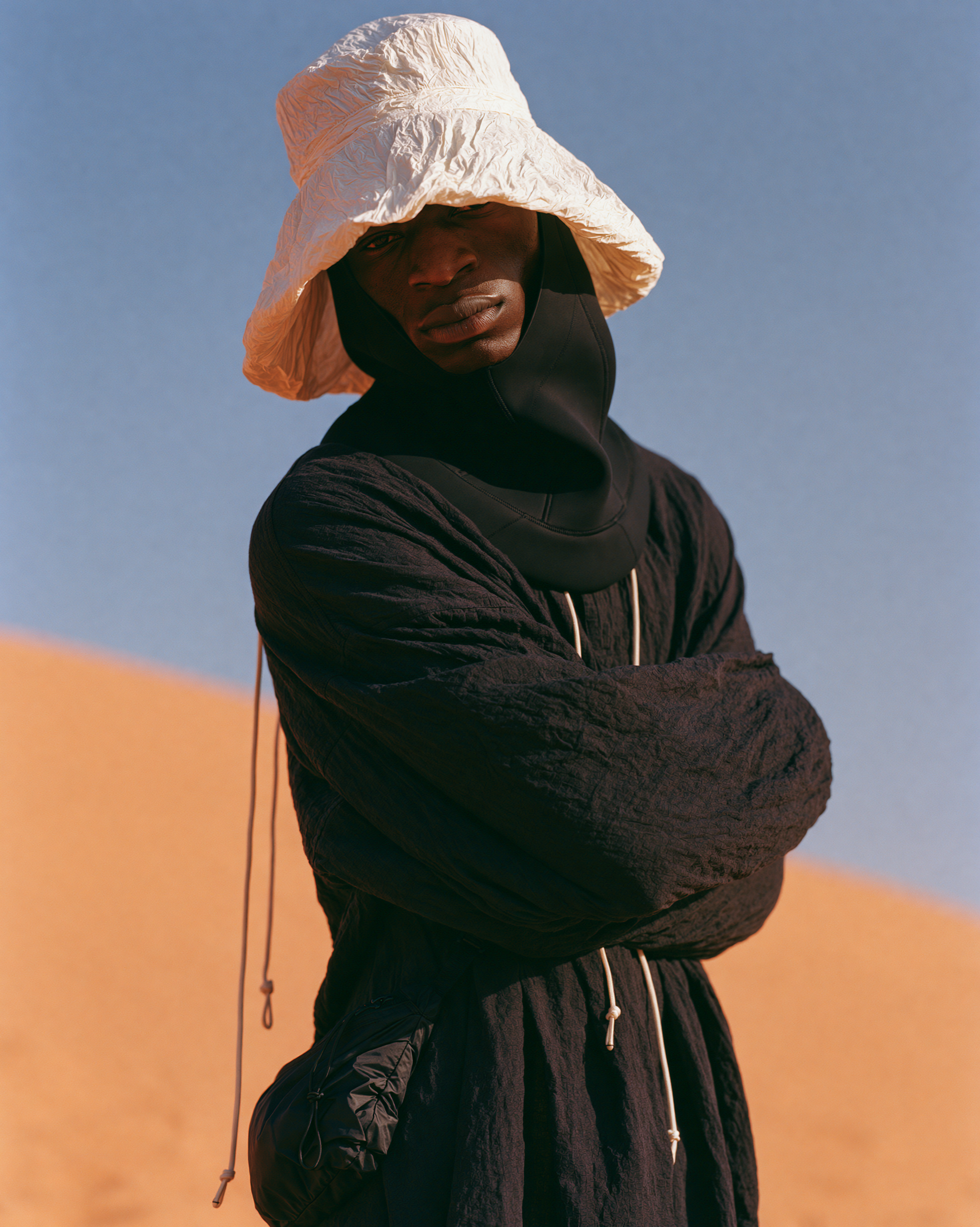 Portrait in a white bucket hat and black quilted garment, arms crossed