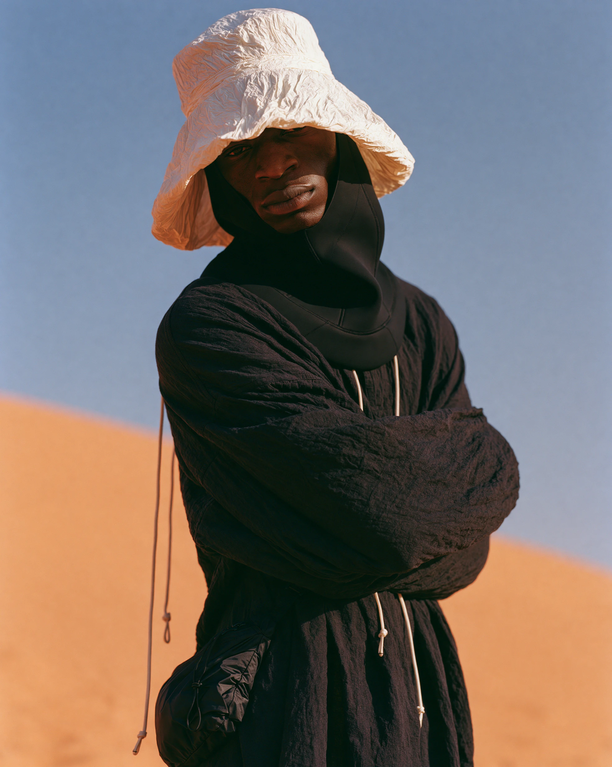 Portrait in a white bucket hat and black quilted garment, arms crossed