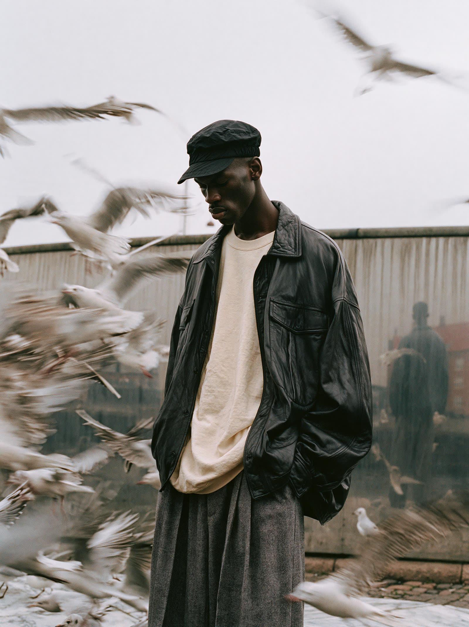 A man walking through a flock of birds by a steel wall