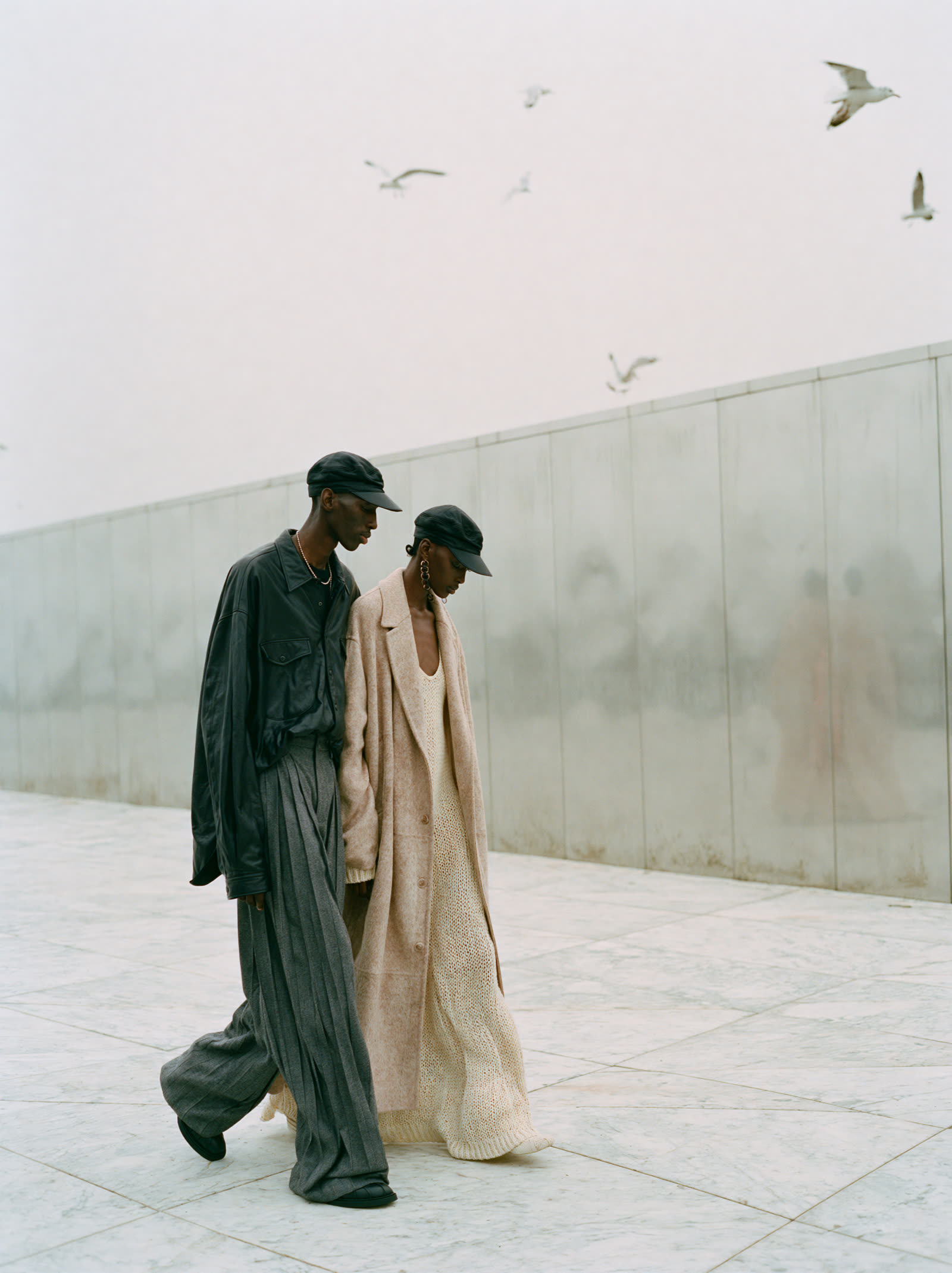 Two models in dark and beige walking along the wall